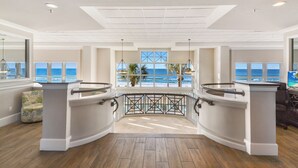 A spacious room with a view of the ocean through large windows, a wooden floor, and a modern ceiling design.