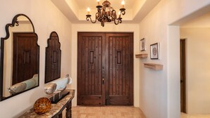 A hallway with a wooden double door, a chandelier, a fish sculpture on a console table, and framed pictures on the wall. - Hacienda Beach Club - 3 bedrooms, 8 people. Can also rent as 2 bedrooms (Cabo San Lucas,)