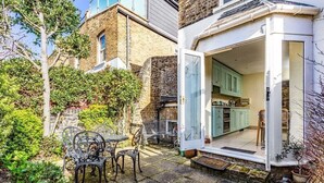 A small, cozy kitchen with a view of the garden, a dining area with a table and chairs, and a brick exterior. - Large Spacious Family Home (sleeps 5), Parsons Green, LONDON (London)