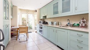 A kitchen with light green cabinets, a dining area with wicker chairs, and a view of the outdoors through glass doors. - Large Spacious Family Home (sleeps 5), Parsons Green, LONDON (London)