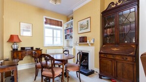 A dining room with a round table and chairs, a fireplace, a bookshelf, and a cabinet with glass doors. - Large Spacious Family Home (sleeps 5), Parsons Green, LONDON (London)