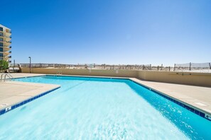 Relax by the pool surrounded by a low deck and a wooden fence, overlooking the beach.