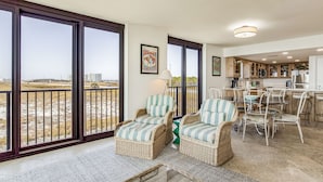 Amplia sala de estar con muebles de mimbre, una mesa de comedor y sillas. Grandes ventanales ofrecen vistas al paisaje.