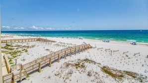 Una playa con un paseo marítimo de madera que llega hasta el agua, arena y vista al océano.