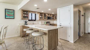 Una cocina moderna con una isla central, taburetes de bar, armarios de madera y un microondas.