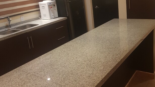 A kitchen with granite countertops, a built-in oven, a refrigerator, and a water dispenser.