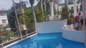 A swimming pool with a white tiled edge, surrounded by palm trees and a white wall with decorative elements.