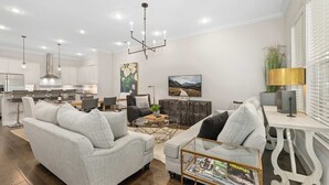 Ein modernes Wohnzimmer mit grauem Sofa, einem Couchtisch und einem Essbereich mit weißem Tisch und Stühlen.