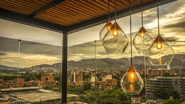 Un interior moderno con grandes ventanales que ofrecen vistas a la ciudad, un sofá de cuero y lámparas colgantes de cristal.