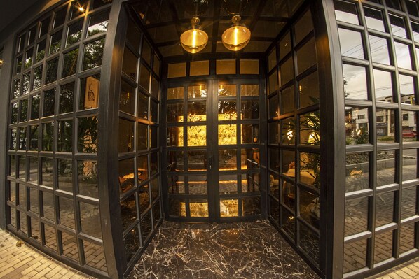 A glass-walled entrance with a marble floor, two hanging lights, and a view of the street outside.