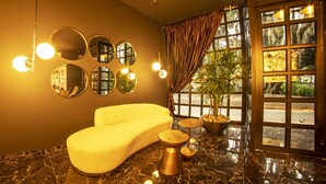 Un baño moderno con un sofá amarillo curvo, piso de mármol y un amplio ventanal con cortinas.