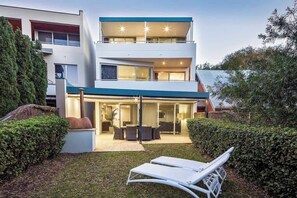 A modern two-story house with a covered patio, a lawn, and a lounge chair. - Azure—Beachside Resort Escape for Groups (Marybrook)