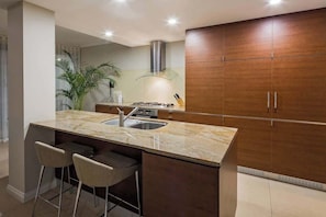A modern kitchen with a central island, bar stools, a stove, and wooden cabinets. - Azure—Beachside Resort Escape for Groups (Marybrook)