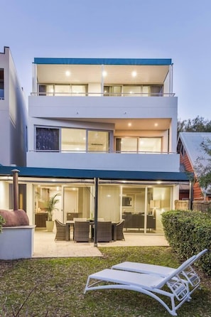 Une maison moderne à deux étages, dotée d’un patio couvert, de mobilier d’extérieur et d’un fauteuil de relaxation.