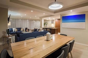 Un salon moderne comprenant un ensemble de canapés, une table à manger avec des chaises, un coin cuisine et un grand tableau accroché au mur.