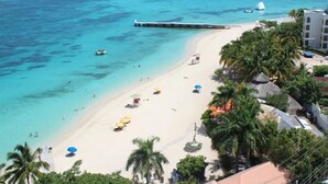 Een strand met helder turquoise water, een steiger en meerdere parasols.