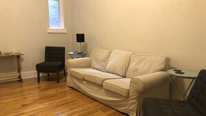 Ein Wohnzimmer mit einem beigen Sofa, einem dunklen Sessel, einem kleinen Tisch und einer Lampe.