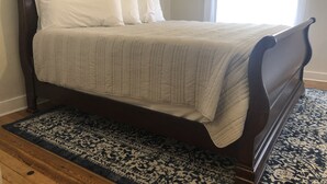 Ein Bett mit dunklem Holzrahmen, einer beigen Steude und weißen Kissen.