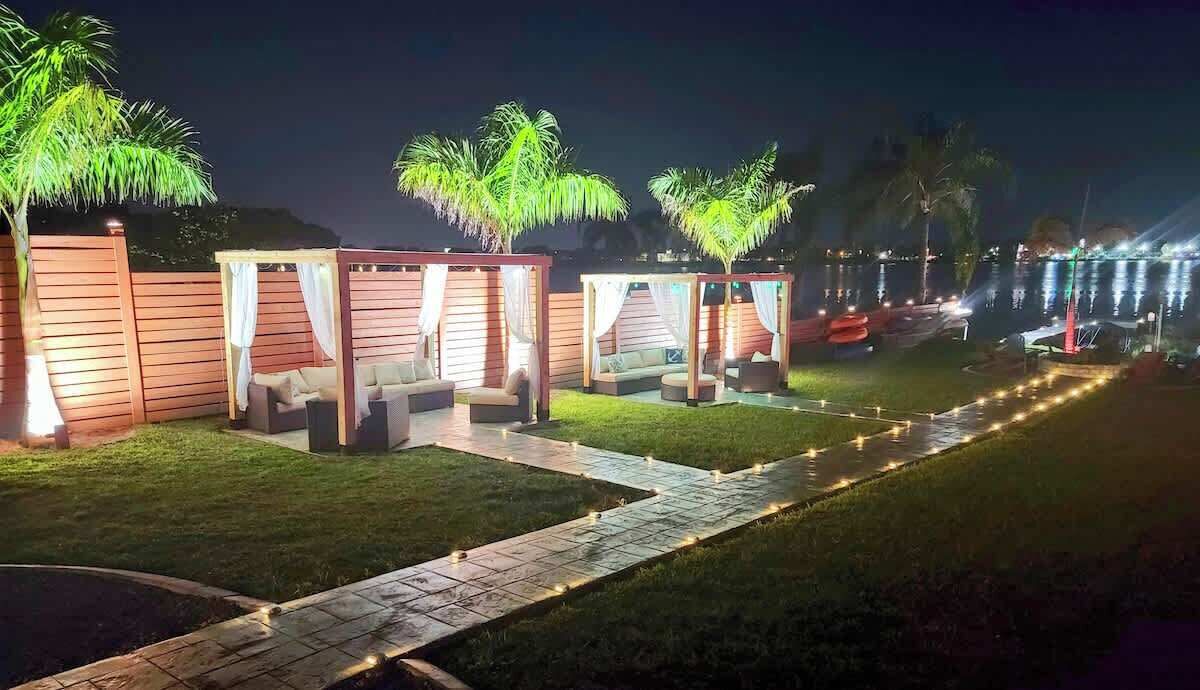 A nighttime outdoor seating area with wooden structures, cushioned seating, and palm trees.