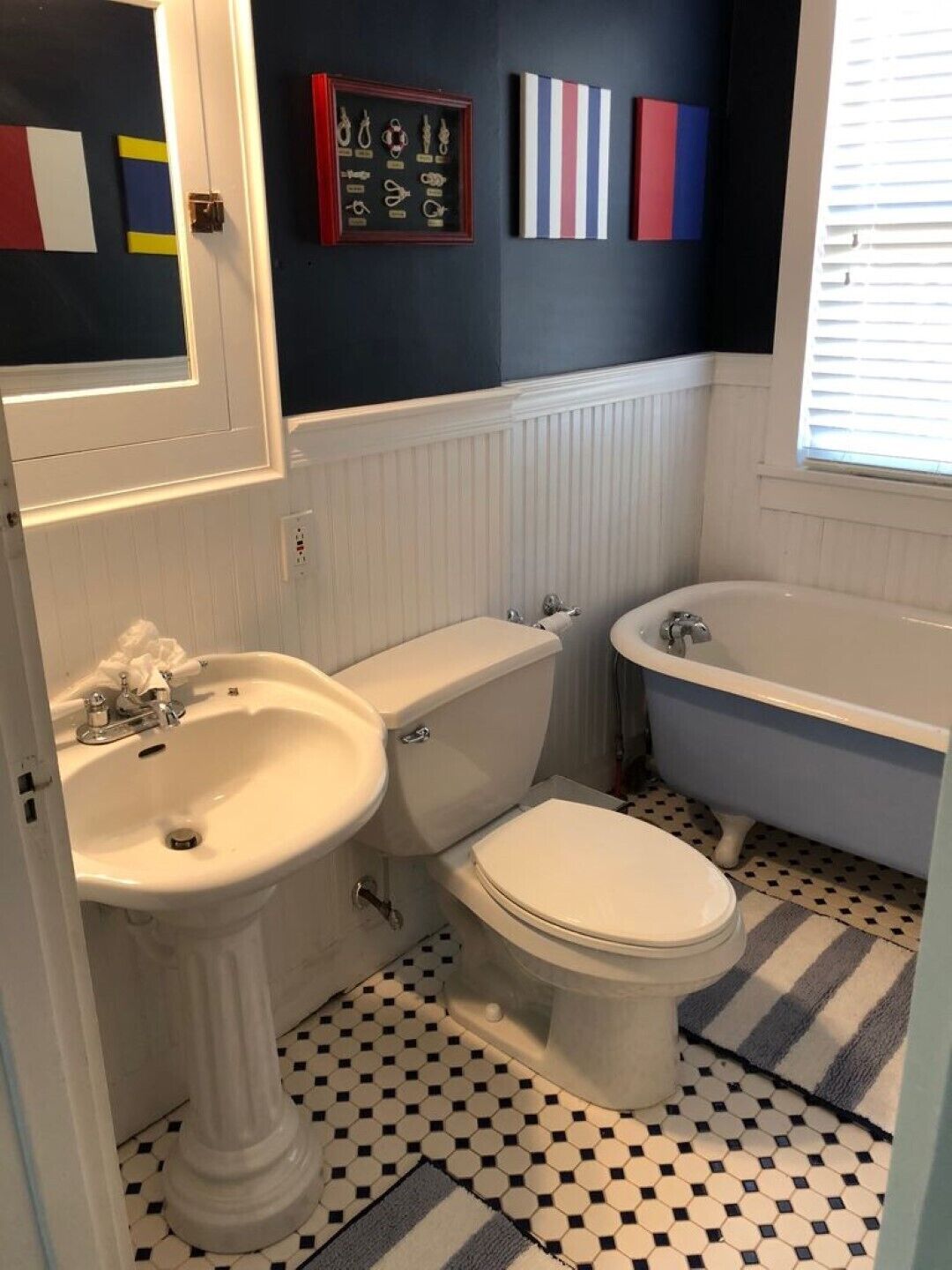 A bathroom with a white sink, toilet, and bathtub. There is a tiled floor and a window with blinds.