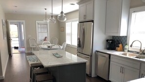 A modern kitchen with a central island, stainless steel appliances, and white cabinetry. - Remodeled 3 bedroom - perfect location for beach trips and beautiful sunsets (south haven)