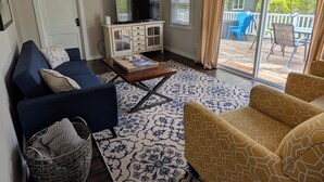 A living room with a blue sofa, a yellow sofa, a coffee table, a TV on a cabinet, and a view of the outdoors through a sliding glass door. - Remodeled 3 bedroom - perfect location for beach trips and beautiful sunsets (south haven)
