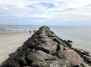 A rocky pier extending into the sea with a sandy beach on one side.