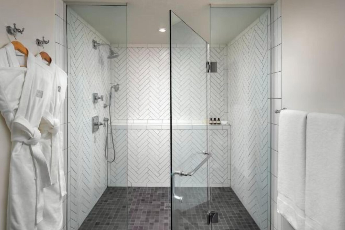 A modern bathroom with a glass shower enclosure, a white tiled herringbone pattern, and a glass door.