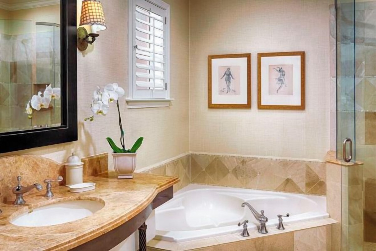 A bathroom with a large mirror, two framed pictures, a sink, a bathtub, and a shower.