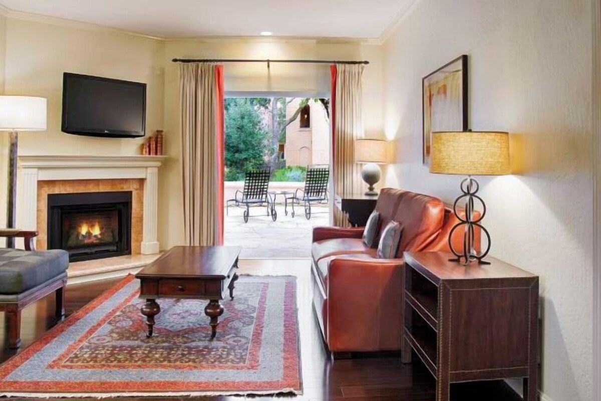 A living room with a fireplace, a television, a sofa, and a view to the outside.
