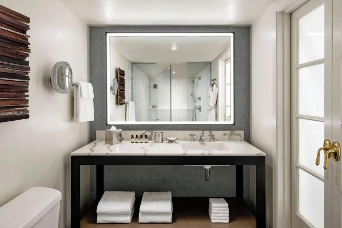 Un baño moderno con un espejo grande, un lavamanos blanco y una ducha con mampara de vidrio.