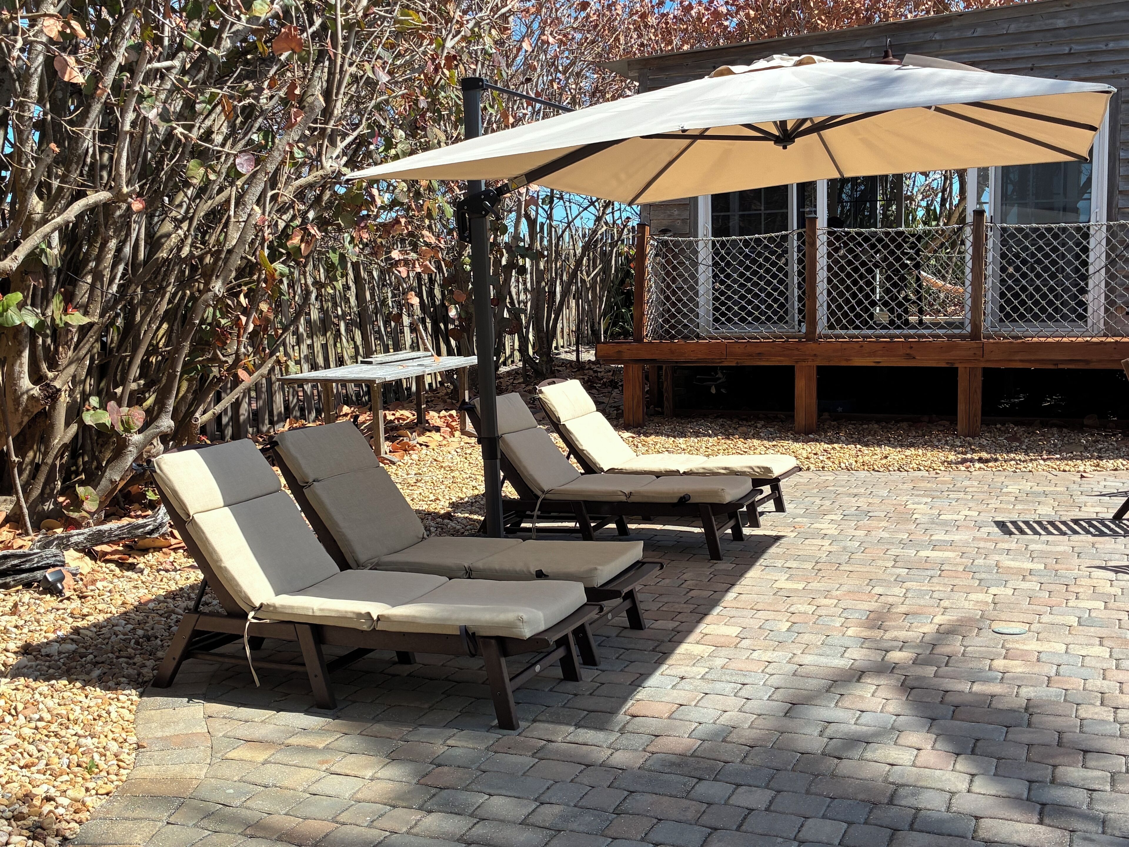 Een terras met lounge fauteuils en een grote parasol, omgeven door een houten terras en een hek van gaas.