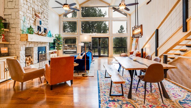 Amplia sala de estar con chimenea de piedra, suelo de madera y una gran mesa de comedor con sillas.