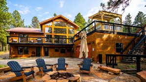 Una cabaña de madera con una amplia terraza, asientos exteriores y una chimenea.