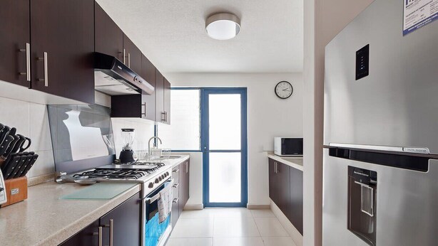 Una cocina moderna con armarios oscuros, electrodomésticos de acero inoxidable y un ventanal grande.