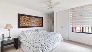 Un dormitorio con cama, mesita de noche, lámpara, ventilador de techo, armario y ventana con persianas.