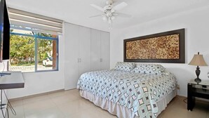 A bedroom with a bed, a desk, a ceiling fan, a window with a view of the outside, and a wall-mounted artwork. - +MS +Espectacular Suite +Alberca Áreas Verdes +9A (Santiago de Querétaro)
