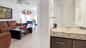 A modern living room with a brown sofa, a coffee table, and a painting on the wall. There is a ceiling fan and a wall-mounted mirror above the sink. - +MS +Espectacular Suite +Alberca Áreas Verdes +9A (Santiago de Querétaro)