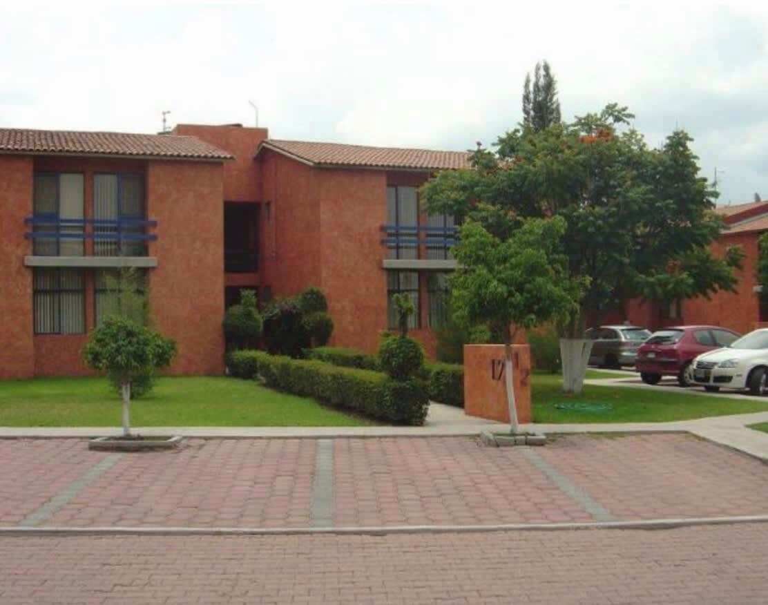 A building with a brick facade, two visible windows with blue blinds, a small tree, and a paved driveway.