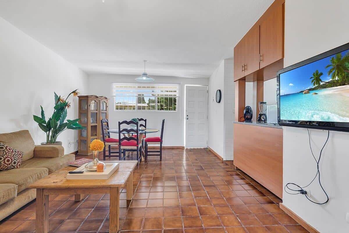 A living room with a sofa, coffee table, and a TV mounted on the wall displaying a beach scene.