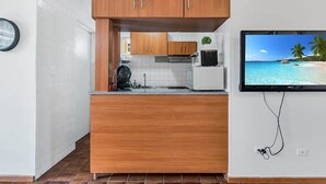 Ett kompakt kök med träskåp, en inbyggd mikrovågsugn och en tv som visar en strandvy.