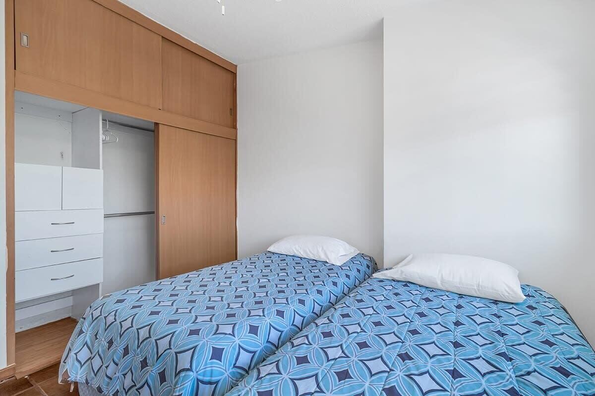 Une chambre à coucher avec un lit, deux oreillers blancs, une armoire en bois et une commode blanche.
