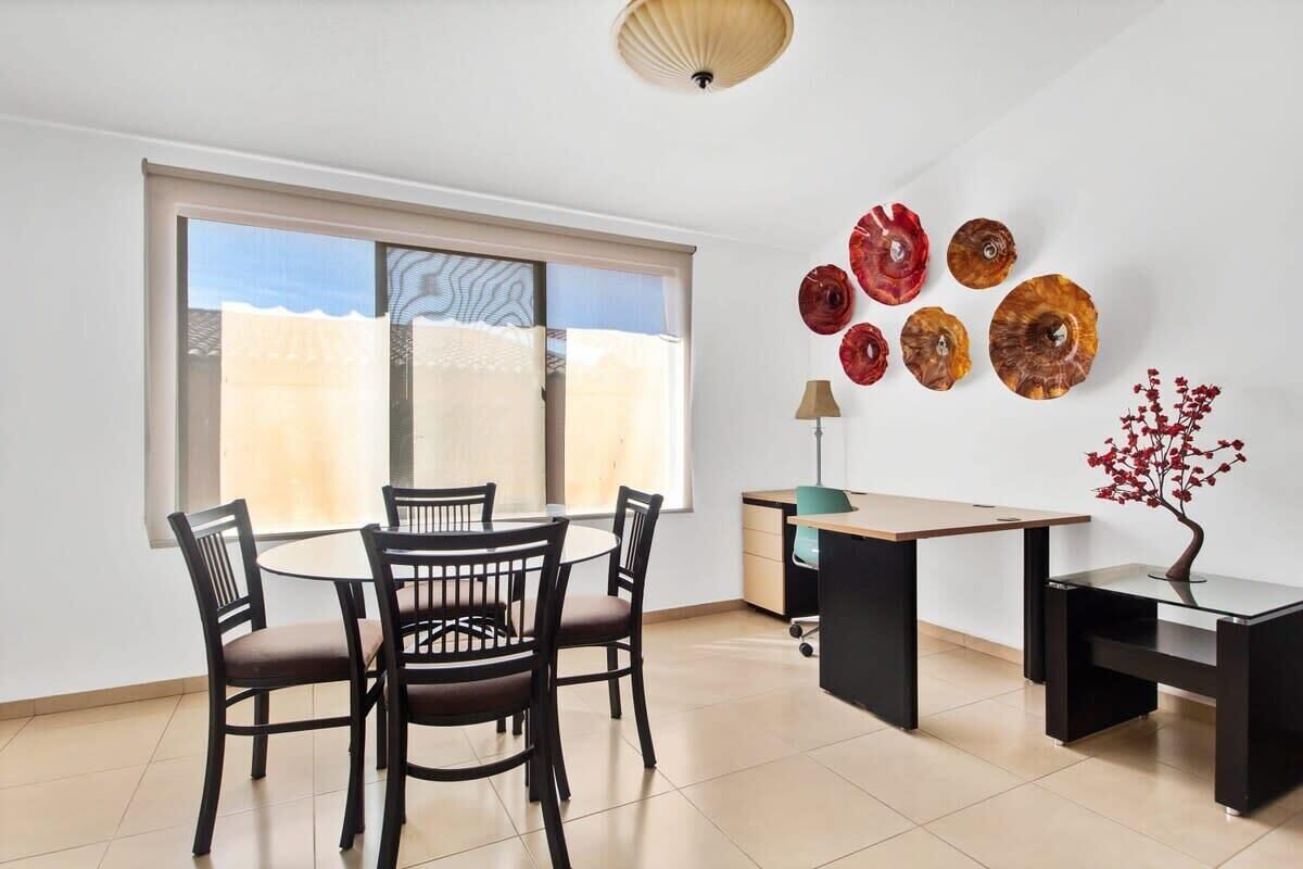 A dining area with a round table and chairs, a desk with a lamp, and decorative plates on the wall.