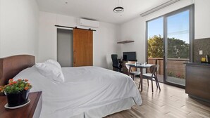 Et moderne hotelværelse med en stor seng, et skrivebord med stol, et fjernsyn og en balkon med udsigt.