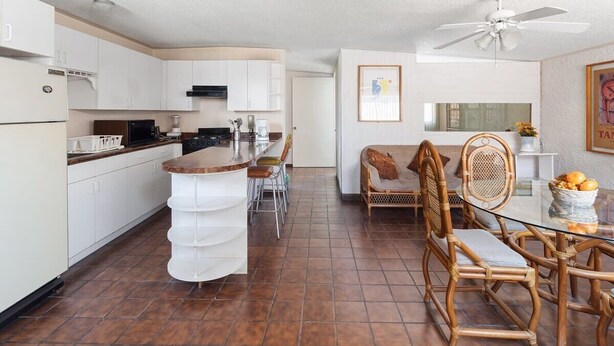 A compact kitchen with white cabinets, a central island, and a dining area with wicker chairs and a glass table.