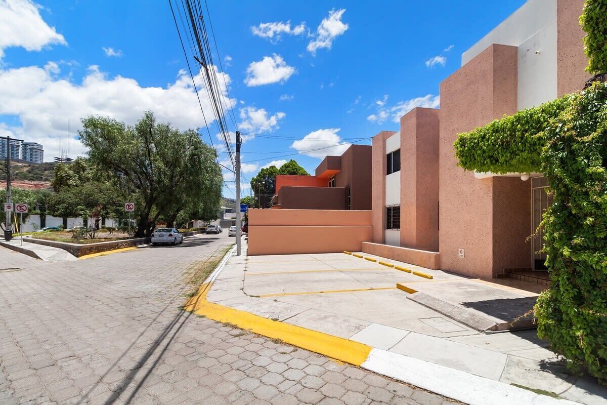 A street view with a building featuring a modern design, a clear sky, and a parking area.