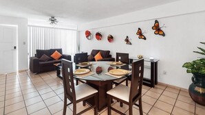 Un coin repas comprenant une table ronde en verre, six chaises et un ventilateur de plafond.