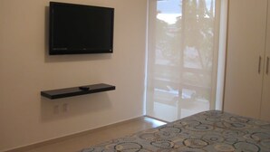A room with a flat-screen TV mounted on the wall, a small shelf below it, a patterned bedspread, and a sliding glass door leading to a balcony. - +MS +Espectacular Suite +Alberca Áreas Verdes +24C (Santiago de Querétaro)