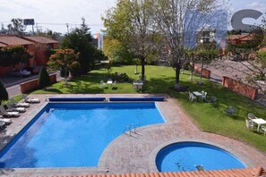 A rectangular swimming pool with a small circular hot tub, surrounded by a brick deck and a grassy area with outdoor furniture. - +MS +Espectacular Suite +Alberca Áreas Verdes +24C (Santiago de Querétaro)