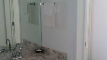 Un baño con lavamanos de mármol, muebles oscuros, inodoro blanco y cabina de ducha con paredes de cristal.